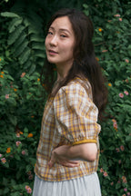 Woman wearing a checkered shirt standing in front of green foliage
